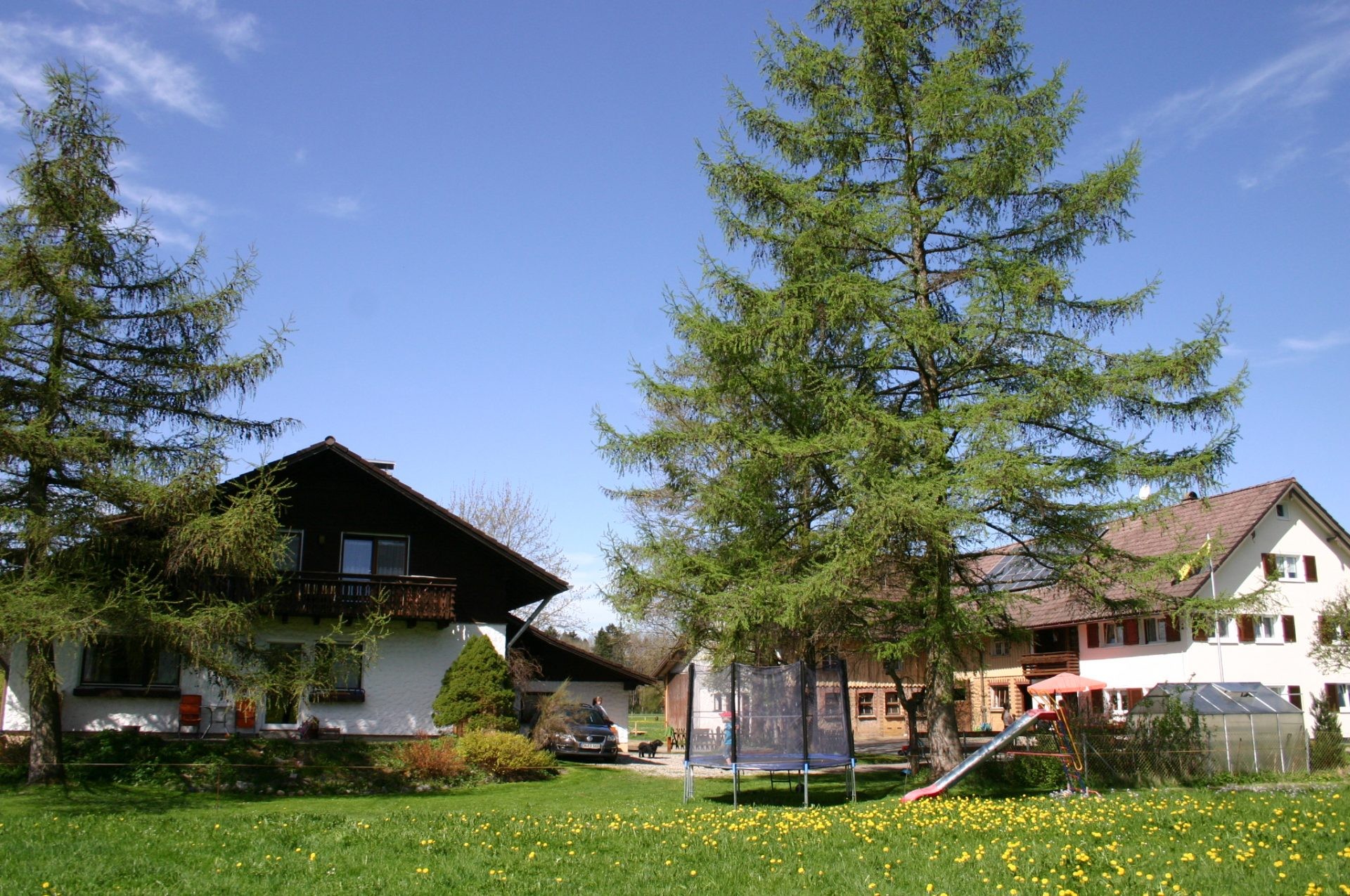 Hofgelände mit Spielwiese, Trampolin und Rutsche zwischen Nebenhaus und weißem Wohnhaus.