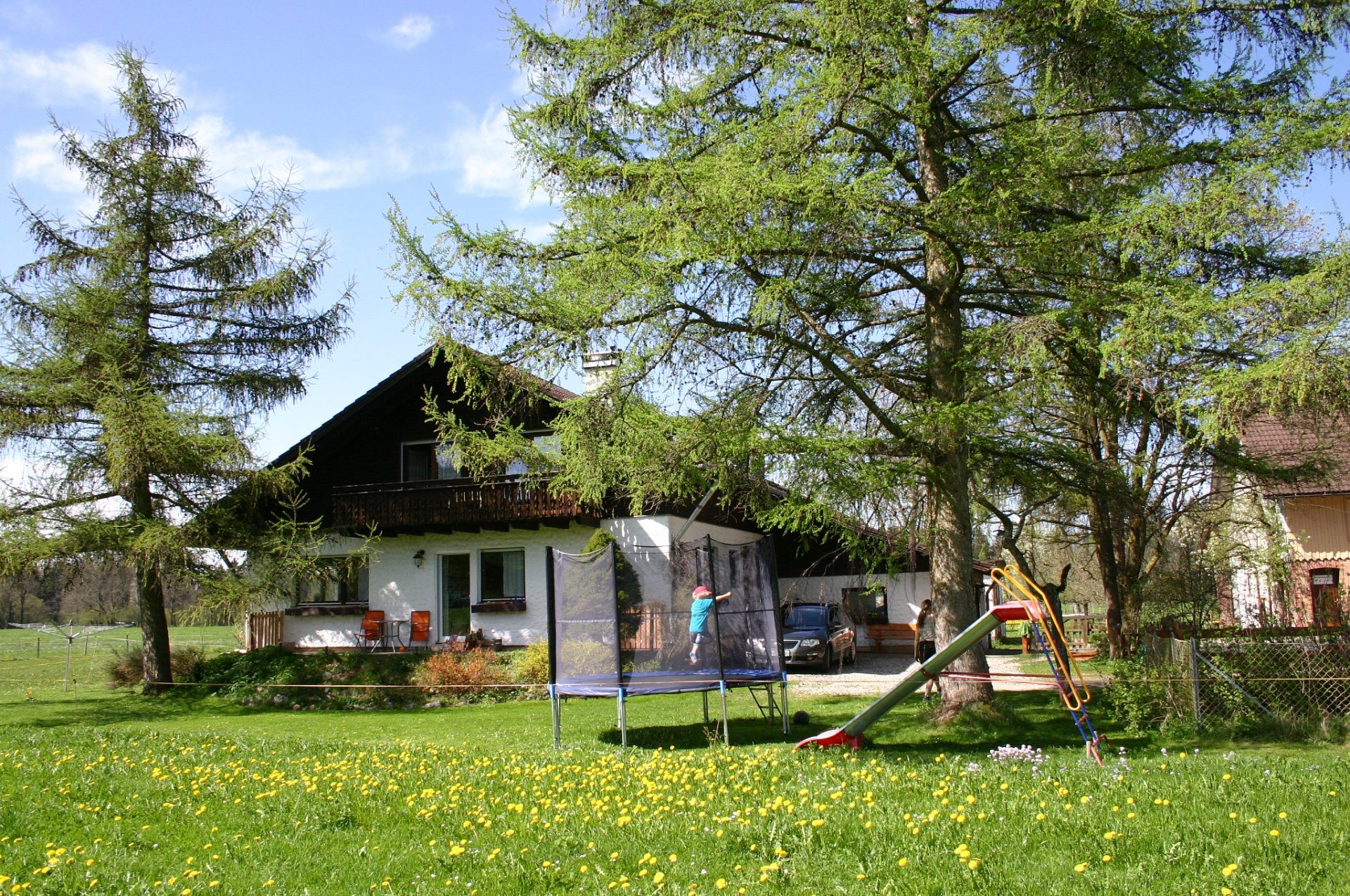 Spielwiese mit Trampolin und Rutsche vor dem Haus mit Holzbalkon.