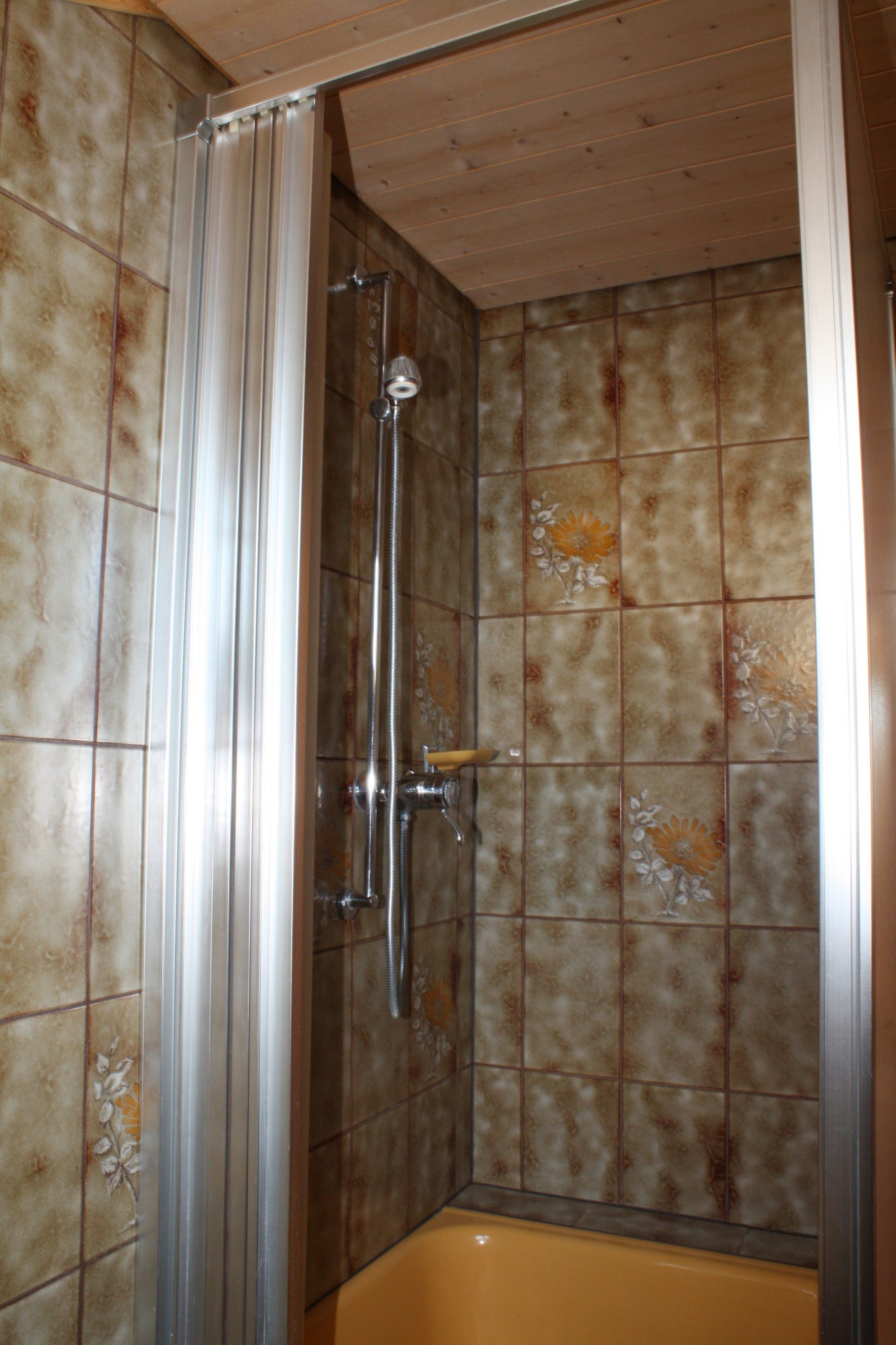 Duschkabine mit Falttür und braun gemusterten Fliesen im Badezimmer.
