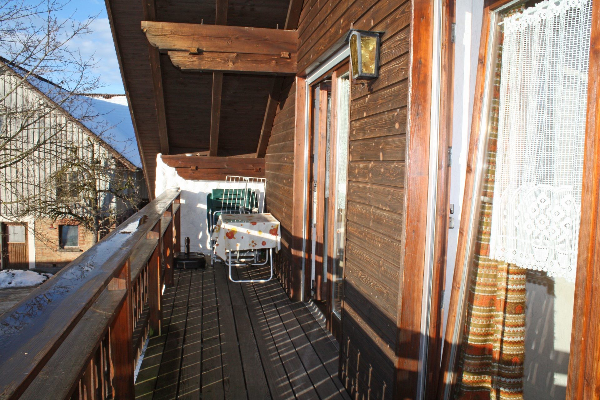 Überdachter Holzbalkon der Ferienwohnung mit Tisch und Stühlen an einem sonnigen Wintertag.