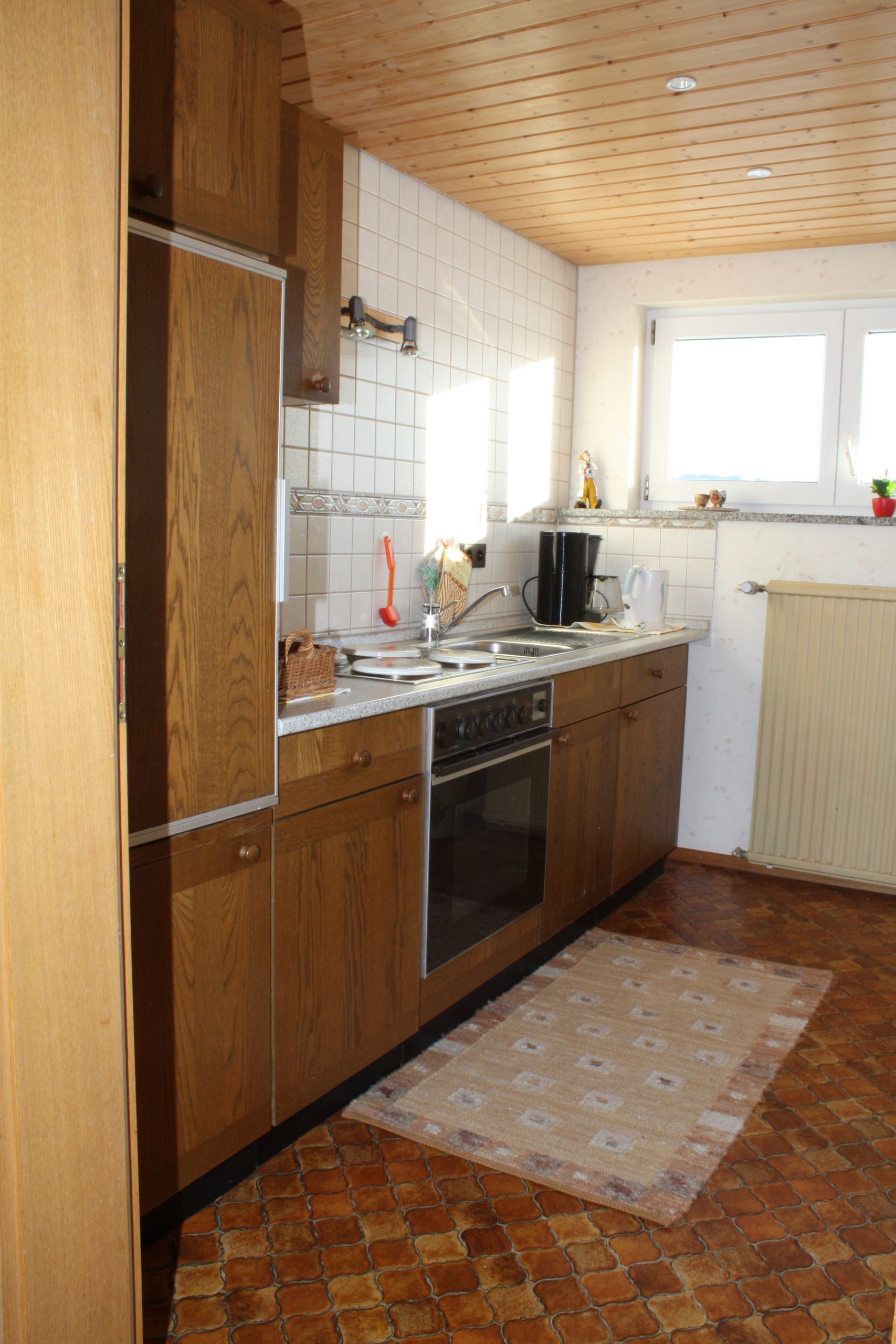 Küche mit Küchenzeile aus dunklem Holz, Backofen, Kochfeld und Kaffeemaschine.