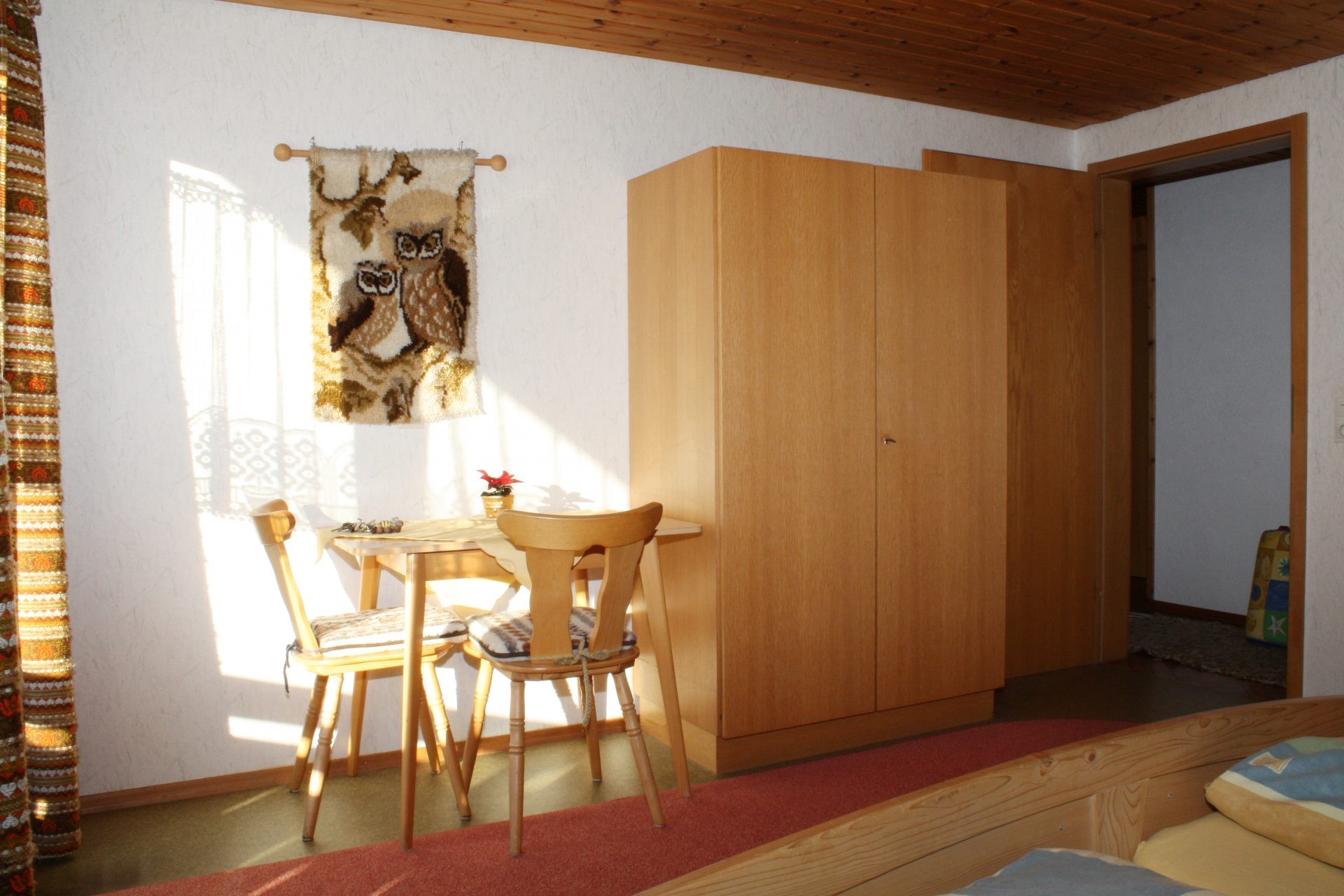 Sonniges Schlafzimmer mit kleinem Tisch, zwei Holzstühlen und einem großen Kleiderschrank.