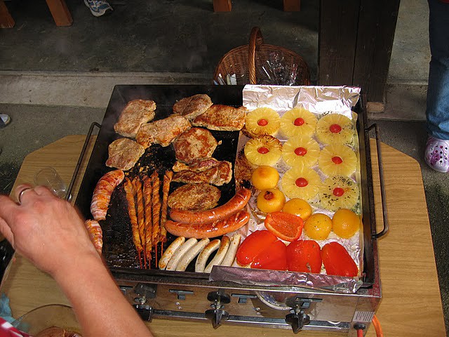 Eine Grillplatte mit Fleisch, Garnelenspießen, Würstchen und gegrilltem Obst.