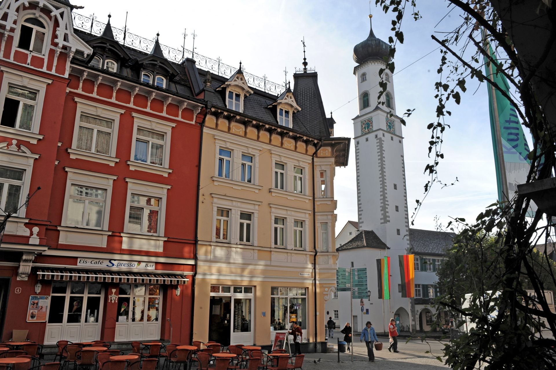 Farbige Gründerzeithäuser mit Eiscafé an einem Altstadtplatz in Isny, dahinter ein weißer Turm mit Zwiebelhaube.