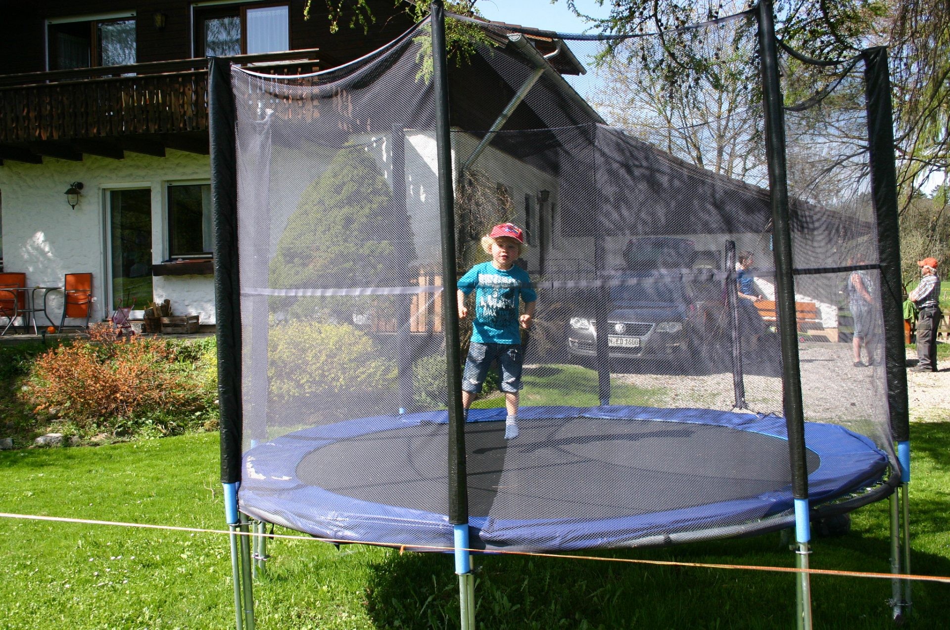 Ein Kind springt auf einem Trampolin mit Netz im Garten vor dem Haus.
