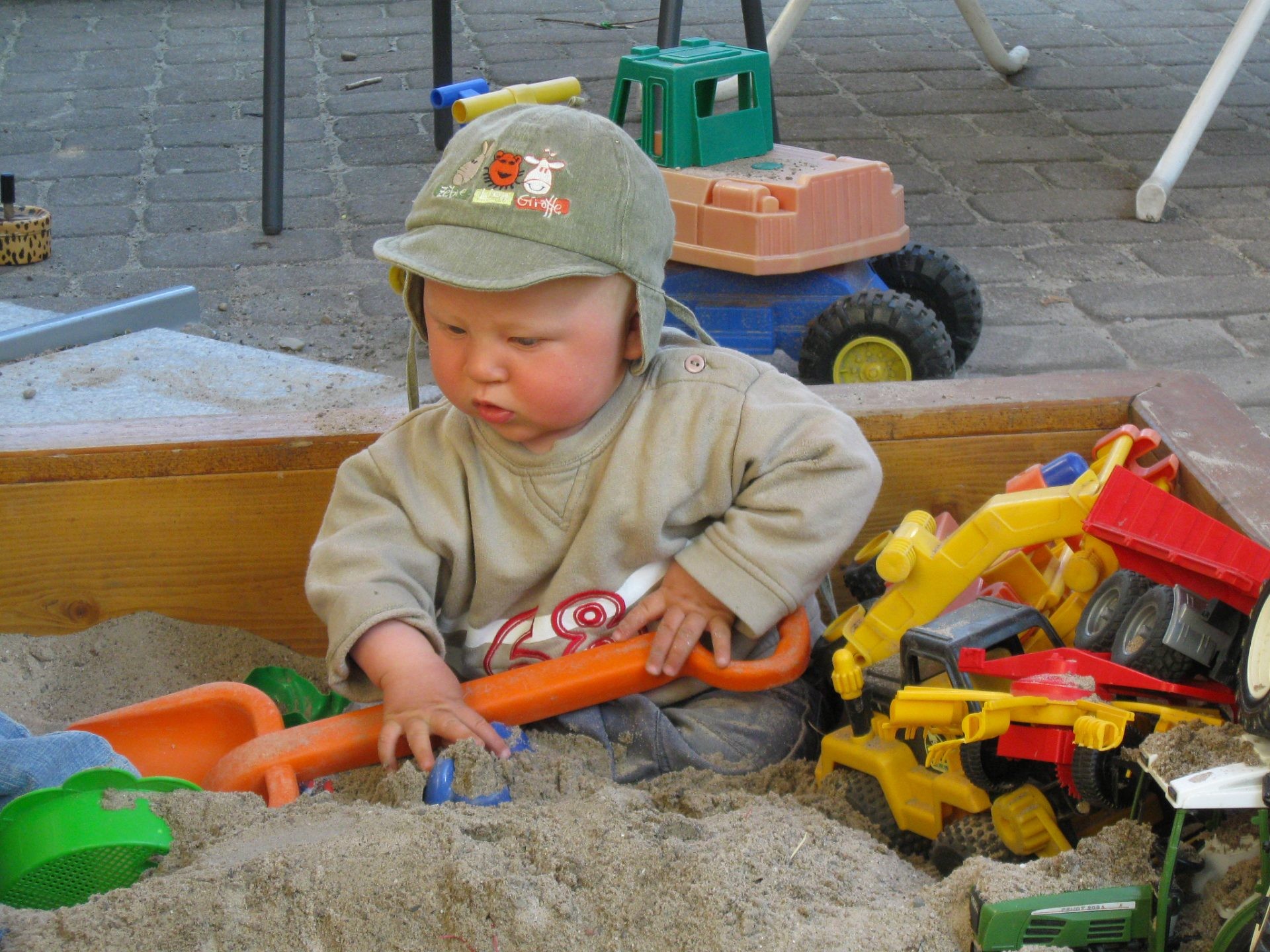Ein Kleinkind spielt im Sandkasten mit Schaufel und Spielzeugbaggern.