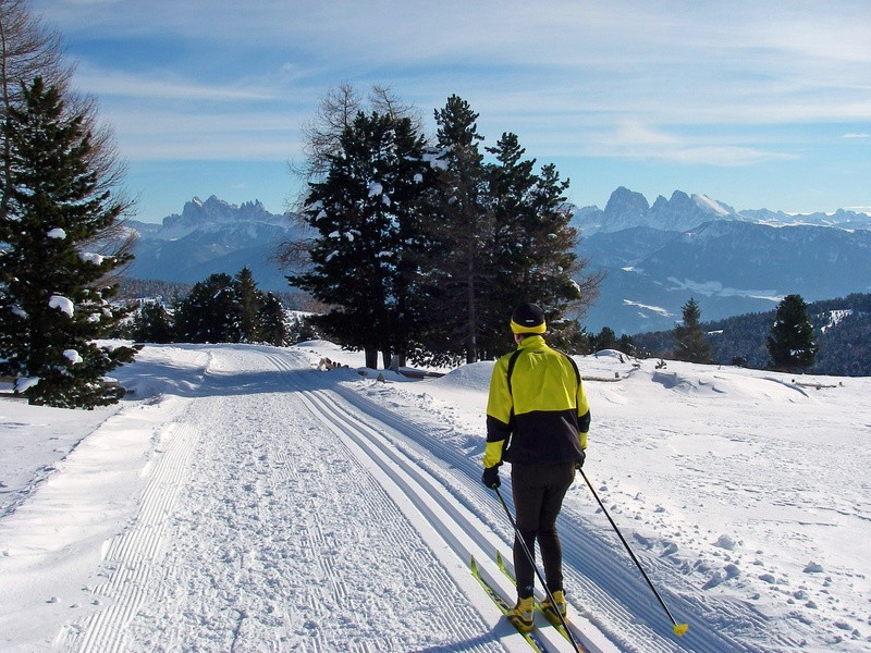 Ein Langläufer auf einer gespurten Loipe vor einem Bergpanorama.